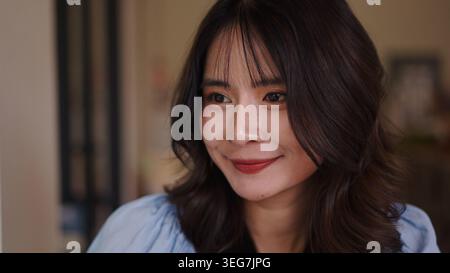 Jeune femme asiatique souriant naturellement à la maison, ressentant de la joie et du contentement Banque D'Images