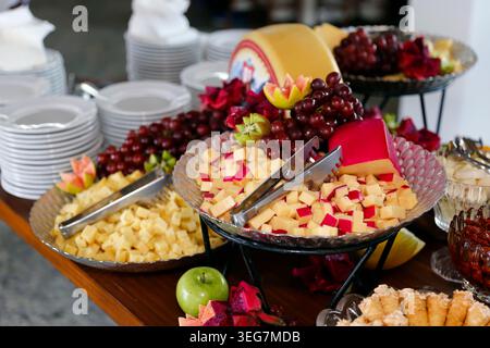 Buffet professionnel avec fromage gouda, cubes, raisins, pommes et kiwi. Servi sur des plateaux en verre avec des stands métalliques, parfait pour les hôtels Banque D'Images