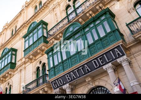 Vue extérieure du Gio. Bâtiment Batta Delia avec sa façade en calcaire, balcons maltais verts traditionnels et panneau commercial à Valette, Sud E. Banque D'Images