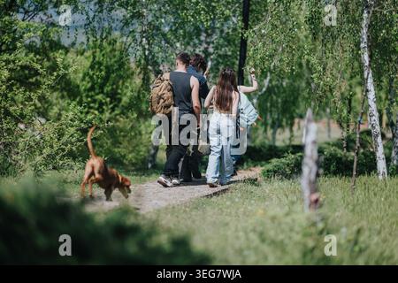 Groupe d'amis randonnée sur un sentier forestier ensoleillé avec un chien et des sacs à dos Banque D'Images
