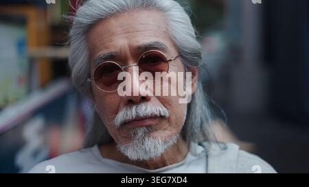 Homme asiatique senior avec de longs cheveux gris et barbe portant des lunettes de soleil rondes Banque D'Images