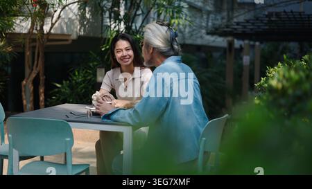 Jeune femme souriante, parlant avec un homme plus âgé à la table de café en plein air Banque D'Images