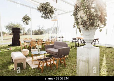 La grande urne blanche contient une végétation luxuriante et des fleurs blanches. Canapé et chaises en bois assis sur l'herbe sous une tente claire. La lumière naturelle filtre à travers le translu Banque D'Images