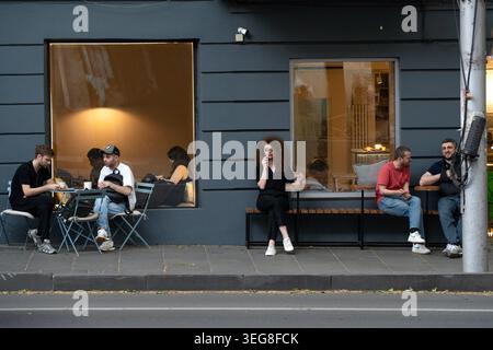 Les gens s'assoient sur des bancs et des tables extérieurs le long d'un trottoir devant un magasin de café. Banque D'Images