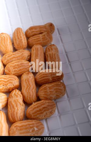 gros plan de pâtisseries à choux de style éclaire doré regroupées sur un plateau carrelé blanc, montrant des textures chaudes striées et des coquillages croustillants sous une douce lumière de studio Banque D'Images