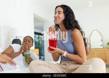 Diverses amies féminines se relaxant sur le lit, sirotant des tasses claires avec des boissons rouges et vertes Banque D'Images