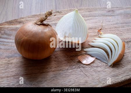 Oignon jaune frais préparé sur une planche à découper rustique en bois avec oignon entier, tranches d'oignon et oignon coupé en deux disposés dans la lumière naturelle de la cuisine Banque D'Images