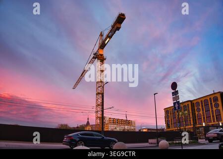 Grue de construction jaune contre un ciel de coucher de soleil rose vibrant à Tallinn Banque D'Images