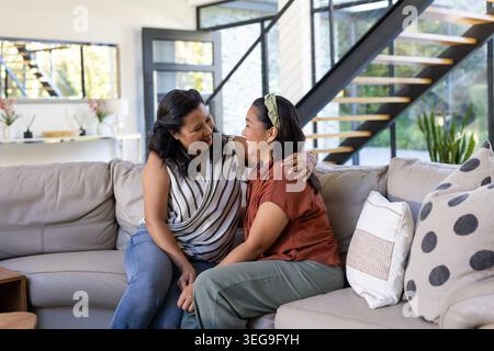 Mère féminine diversifiée et fille assise sur le canapé sectionnel beige dans le salon, souriant Banque D'Images