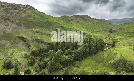 Une vue aérienne capture une vallée verdoyante avec des collines ondulées, des murs de pierre traditionnels et une parcelle dense d'arbres entourant quelques dwelli isolés Banque D'Images