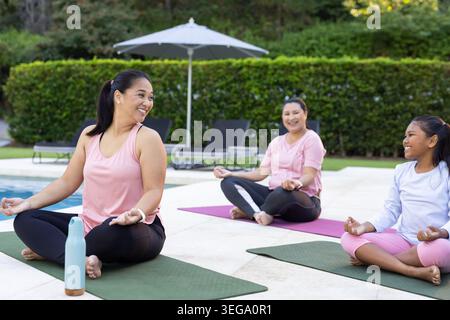 Diverses amies féminines portant rose et noir assis sur la terrasse de la piscine faisant du yoga avec des tapis Banque D'Images