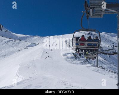Une scène hivernale à la Thuile, montrant un télésiège pour quatre personnes montant une pente enneigée, avec des skieurs descendant la piste damée sous un vide Banque D'Images