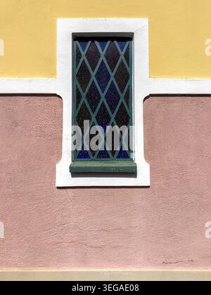 Une vue verticale d'un extérieur de bâtiment vibrant avec une fenêtre en forme de losange bleu sertie sur stuc rose et jaune. La lumière du soleil emphasi Banque D'Images