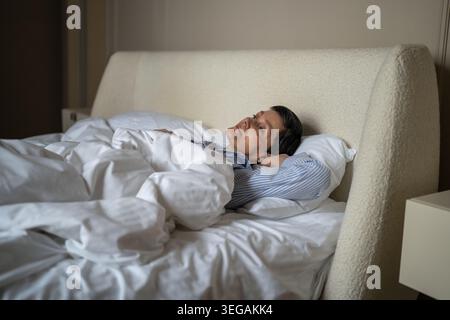 Reposé positive femme senior profitant d'un matin lent couché dans un lit confortable dans la chambre à coucher à la maison. Banque D'Images