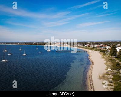Cette superbe photographie aérienne capture un paysage côtier serein avec une marina parsemée de voiliers. L'image présente un bea de sable immaculé Banque D'Images