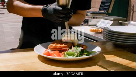 Verser la gaufre à la sauce hollandaise servant les mains d'oeufs Banque D'Images