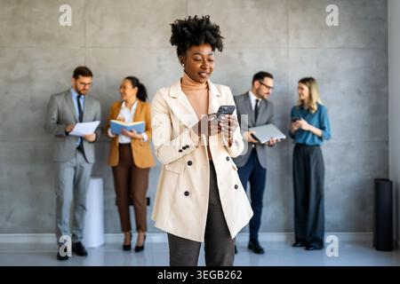 Une femme d'affaires confiante mène sa vie de bureau occupée, multitâche avec la communication smartphone Banque D'Images