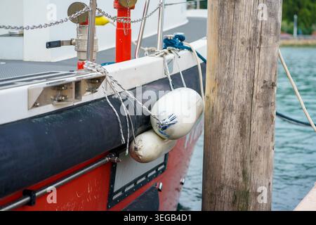 Gros plan de l'aile de bateau attachée à la coque près du poteau de quai, illustrant l'équipement de protection marine, les détails d'amarrage et le concept de sécurité nautique. Banque D'Images