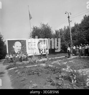 Sloviansk, 1983 ans, Slavkurort, camp des pionniers Vishnegorsk. Une cérémonie solennelle de levée de drapeau a lieu à l'extérieur avec un petit groupe d'enfants debout à l'attention. Certains garçons tiennent des tambours, tandis qu'une fille lève le drapeau sur un grand poteau à côté d'un grand panneau d'affichage soviétique représentant le portrait de Lénine. Une photographie d'archives historique en noir et blanc capturant l'atmosphère authentique de l'époque, les traditions patriotiques des organisations de jeunesse socialistes et le Donbass paisible. Banque D'Images