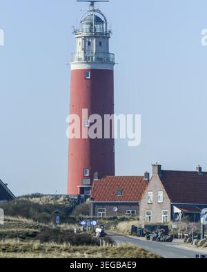 Un phare est visible près d'un petit village au bord de l'eau. Les gens font du vélo sur la route. Les maisons sont vues à proximité sous un ciel dégagé. C'est une journée ensoleillée Banque D'Images
