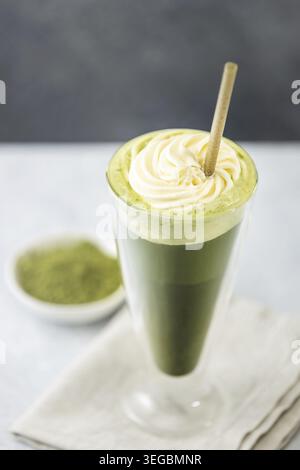 Latte matcha congelé rafraîchissant garni de crème fouettée et servi avec une paille écologique qui favorise un LIF sain et durable Banque D'Images