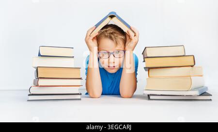 garçon souriant avec beaucoup de livres tient le livre comme un toit au-dessus de sa tête. Concept de sécurité dans l'apprentissage. Banque D'Images