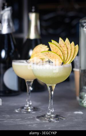 Deux cocktails alcoolisés de pommes vertes servis dans des verres coupés avec des garnitures de fruits en éventail sur un comptoir de bar sombre. Banque D'Images