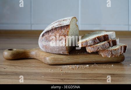Pain croustillant rustique fraîchement cuit avec plusieurs tranches coupées sur un bureau de hachage. Préparation alimentaire traditionnelle biologique dans l'intérieur de la cuisine domestique. Côté Banque D'Images
