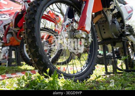 Gros plan d'une roue à rayons avant sur une moto de vélo de terre orange avec un pneu à cliquetis et un disque de frein ondulé dans un paddock extérieur. Roue avant de Banque D'Images