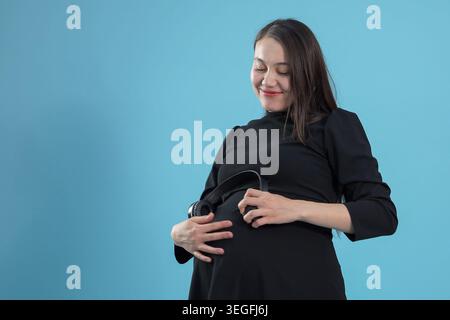 Heureuse femme asiatique enceinte tenant son ventre debout sur fond Banque D'Images