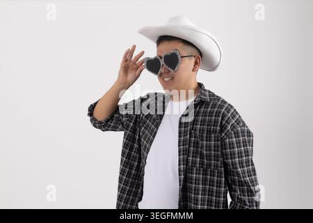 Jeune homme beau portant un chapeau de cow-boy ajustant les lunettes de soleil regardant de côté Banque D'Images