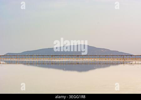 Une longue passerelle en bois traverse les eaux cristallines du lac Karum en Éthiopie. La structure est parfaitement reflétée sur la surface du lac salé, avec Banque D'Images