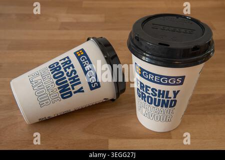 Deux tasses à café Greggs ou tasses avec du café Fairtrade fraîchement moulu imprimé sur le devant, un sur son côté sur le comptoir en bois Banque D'Images