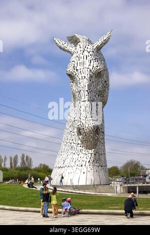 Une jeune famille visitant les Kelpies à Falkirk, en Écosse, sous l'une des sculptures géantes de tête de cheval par une journée ensoleillée. Banque D'Images