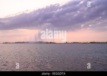 Touristes marchant sur la Corniche de Djeddah au coucher du soleil avec la fontaine du roi Fahd qui se lève sur la mer Rouge en Arabie Saoudite Banque D'Images
