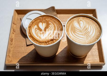Deux lattes avec art Latte coeur dans des tasses en papier sur plateau en bois, café à emporter Banque D'Images