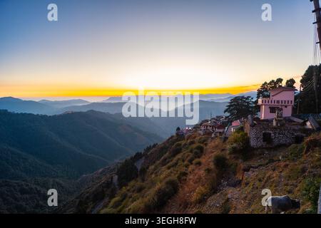 Une vue panoramique de la chaîne de montagnes de l'Himalaya pendant un lever de soleil doré avec un petit village perché sur la crête à Chakrata, Uttarakhand, Inde. Banque D'Images