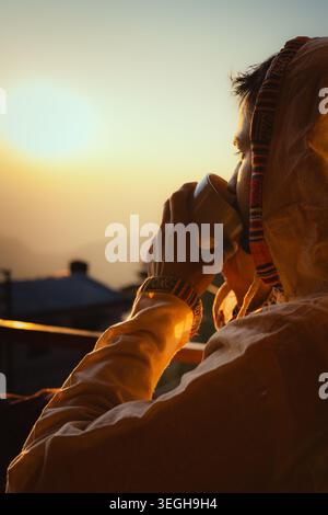 Une personne profite d'une tasse de thé chaude tout en regardant le lever du soleil doré sur le paysage de montagne pittoresque à Chakrata, Uttarakhand, Inde. Banque D'Images