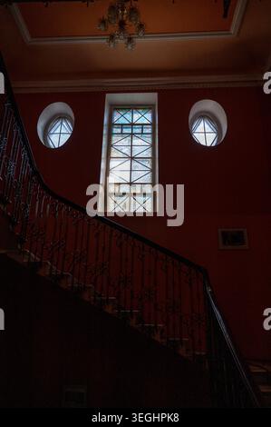 Escalier en marbre et balustrades en fer ornées à l'intérieur d'un bâtiment historique. Grande fenêtre cintrée fournit Banque D'Images