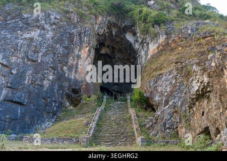 D'anciennes marches en pierre mènent à une entrée sombre de grotte. Des falaises accidentées entourent le passage étroit. La mousse verte pousse sur les surfaces rocheuses altérées. Cave Mo Banque D'Images