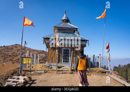 Une personne se tient devant un temple de pierre historique orné de drapeaux orange sous un ciel bleu clair dans les montagnes de Chakrata, Uttarakhand, Inde. Banque D'Images