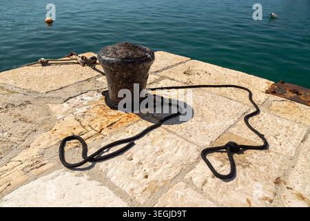 Borne d'amarrage en métal rouillé avec corde noire sur une jetée en pierre à Rovinj, Croatie. Banque D'Images