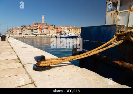 Corde épaisse attachée à une borne d'amarrage noire fixant un bateau rouillé bleu à un quai de pierre à Rovinj, Croatie. Banque D'Images
