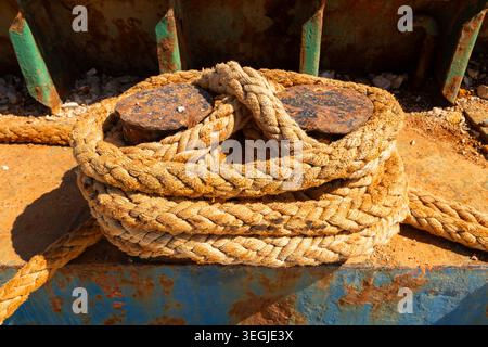 Gros plan d'une corde d'amarrage enroulée attachée autour de bornes en métal rouillé à un petit quai dans le port de Rovinj, Croatie. Banque D'Images