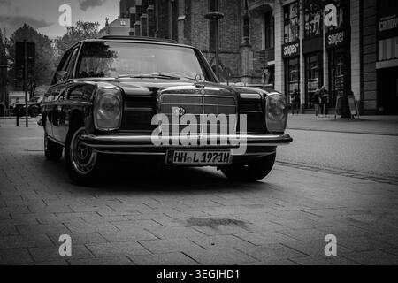 Vue en noir et blanc sur la rue d'une Mercedes-Benz classique d'époque garée à Hambourg, en Allemagne, avec une architecture urbaine, des devantures de magasins et une ville de mauvaise humeur Banque D'Images