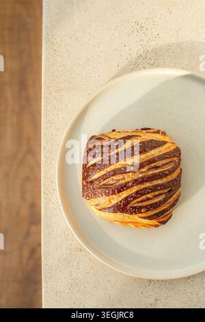 Gros plan de haut en bas d'un croissant au chocolat bicolore fraîchement cuit avec des couches de pâtisserie laminées proéminentes sur une plaque en céramique blanche. Banque D'Images