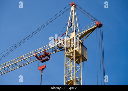 Gros plan détaillé d'une cabine de grue à tour industrielle jaune, d'un mécanisme de poulie et de câbles en acier sur un fond de ciel bleu vif. Banque D'Images