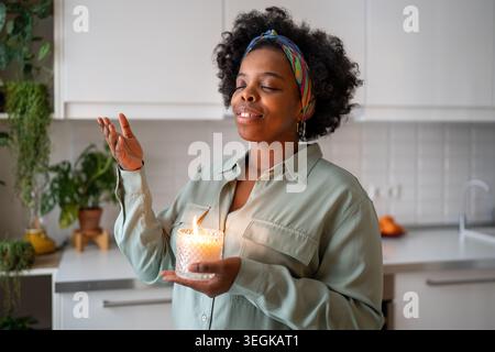 Femme noire calme inhalant profondément un parfum de bougie aromatique incandescente, méditant, pratiquant la respiration. Banque D'Images