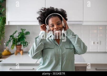 Femme joyeuse écouter de la musique avec des écouteurs souriant avec insouciant, stimulant l'humeur, regarde la caméra Banque D'Images