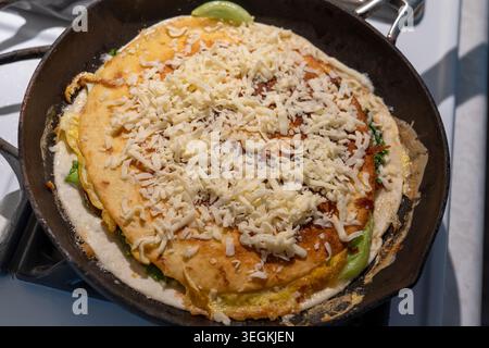 Une photographie en gros plan en grand angle capturant l'étape d'ajout d'une autre couche de fromage râpé sur une tortilla grillée pour le petit déjeuner. Un montant généreux Banque D'Images